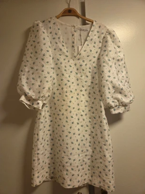 Vit blommig klänning Samsøe Samsøe - Supersöt vit kortklänning från Samsøe Samsøe med små gröna blommor, puffiga trekvartsärmar och v-ringning. Klänningen har en lätt struktur i tyget. Perfekt för sommarens alla tillfällen!