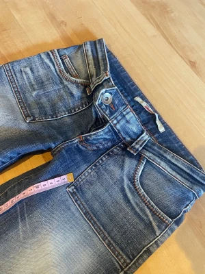 Lågmidjade jeans - Midja: ca 38 cm. Innebenslängd: ca 78 cm. Toppen skick utöver små slitningar längst ner samt en liten fläck, Se bilder. Säljer även andra lågmidjade jeans i min profil