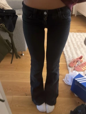 Svarta bootcut jeans med slitna benslut - Säljer ett par svarta bootcut jeans med låg midja och slitna benslut för en avslappnad vibe. Jeansen har klassisk femficksmodell och är tillverkade i stretchigt denimtyg som sitter snyggt. Perfekta för dig som gillar en trendig och bekväm look.