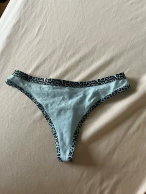 Ljusblå trosa med leopardkant - ALDRIG ANVÄNDA! Säljer en ljusblå trosa i mjukt material med leopardmönstrade kanter i svart, vitt och rosa. Modellen är lågmidjad och har en klassisk trosa-form som sitter bekvämt. Perfekt för dig som gillar djurmönster och vill ha något unikt i underklädeslådan.