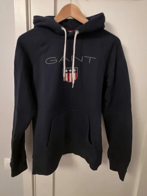 Mörkblå hoodie från GANT - Mörkblå hoodie från GANT med stort tryck på framsida.