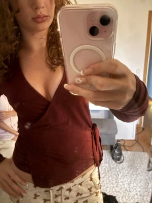 Vinröd omlottopp med knytband - Säljer en vinröd omlottopp med långa ärmar och knytband i midjan. Toppen har en djup v-ringning och är gjord i ett mjukt, stretchigt material som sitter snyggt på kroppen. Perfekt för dig som gillar en stilren men ändå trendig look.