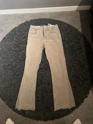Beiga bootcut jeans från Zara - Säljer ett par beiga bootcut jeans från Zara i storlek 38. Jeansen har råa, fransiga benslut och klassisk femficksmodell. Tillverkade i ett mjukt denimtyg med lätt slitna detaljer för en avslappnad look.
