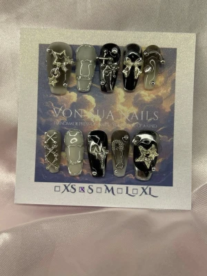 SilverK (S); Medium Coffin - Unika handgjorda press-on naglar i svart och vitt med coola silverdetaljer som stjärnor och säkerhetsnålar. Mix av handmålat, dekorerade med 3D-metallaccessoarer. Perfekt för dig som vill sticka ut med edgy och trendig nageldesign.S: 15 mm, 11,5 mm, 12 mm, 11 mm, 9 mm 