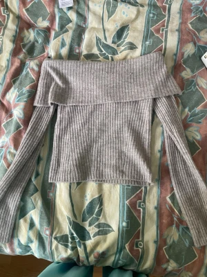 Ljusbeige ribbad offshoulder topp - Trendig ljusbeige (ser ljusgrå ut i ljuset) ribbad offshoulder topp med långa ärmar från HM. Toppen har en bred kant över axlarna och är tillverkad i ett mjukt stickat material som ger en snygg och bekväm passform. Det är inget stickigt typ o perfekt  för dig som vill ha en stilren och enkel look. Pris går att diskutera!!