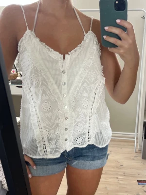 Miss Me Topp - Söt vit topp från Miss Me med tunna axelband, broderade blommönster och volangdetaljer längs kanterna. Toppen har knappar framtill. Lätt och luftig.