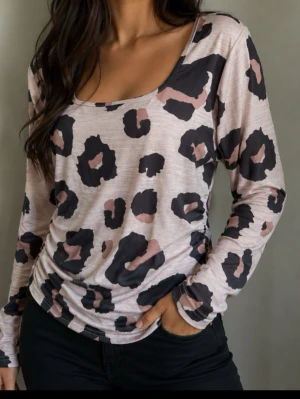 Leopardmönstrad långärmad topp strl XL - Trendig långärmad topp med leopardmönster i svart och beige  Toppen har en rundad, djup urringning och är tillverkad i ett mjukt, stretchigt material som sitter snyggt mot kroppen. Perfekt för dig som vill sticka ut med ett djuriskt print. Lite drapering i sidorna se bild 