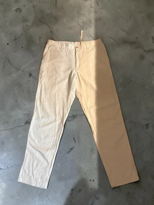 Beige linnebyxor med resårmidja - Snygga beige linnebyxor med rak passform och resår i midjan samt dragsko. Byxorna har knappgylf och en bakficka med knapp. Perfekta för en avslappnad och stilren look. Materialet är svalt och luftigt linne.