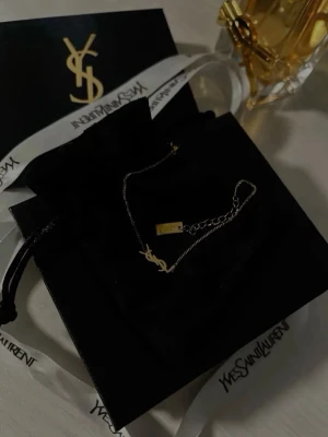 Armband  - Snyggt armband  från Yves Saint Laurent med den ikoniska YSL-loggan i guld. Kedjan är tunn och elegant, och armband har en justerbar längd. Perfekt accessoar för att lyfta vilken outfit som helst.