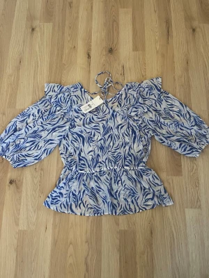 Blåvit blus med puffärm och knyt helt ny med lapp på - Säljer en blåvit blus med zebramönster och puffiga långärmar. Blusen har knyt i nacken och markerad midja för en feminin siluett. Tunt, luftigt material som passar perfekt till varmare dagar. Supersnygg till både jeans och kjol!
