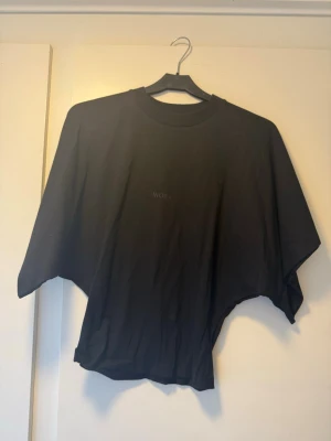 Svart fitted t-shirt från Avora - Säljer en svart fitted t-shirt från Avora med diskret logga på bröstet. T-shirten har bred passform och korta ärmar, perfekt för en avslappnad och trendig look. Tillverkad i mjuk bomull som känns skön mot huden.