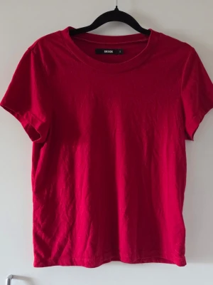Röd basic t-shirt - En enkel röd t-shirt. Klassisk rund halsringning, korta ärmar och lite tajtare passform. Perfekt till jeans eller shorts för en avslappnad look.