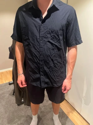 Svart kortärmad skjorta - En enkel svart skjorta med korta ärmar och klassisk krage. Skjortan har knappar framtill och en bröstficka. Perfekt till sommaren och lätt att matcha med olika outfits.