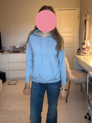 Ljusblå hoodie med huva - En enkel och stilren ljusblå hoodie med huva och dragsnören. Hoodien har en avslappnad passform och ribbade muddar vid ärmar och nederkant. Perfekt för en chill och bekväm look. Materialet ser ut att vara mjukt och skönt, troligen bomullsblandning.