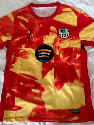 Barcelona matchtröja röd/gul Nike - Säljer en Barcelona matchtröja från Nike i röd och gul tie-dye design. Tröjan har klubbmärke, Nike-logga och sponsortryck på bröstet samt UNHCR-logga på ryggen. Tillverkad i lätt och ventilerande material, perfekt för fotboll eller träning.