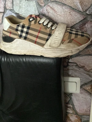Burberry  sneakers - Snygga sneakers från Burberry med klassiskt beige, svart och rött rutmönster. Skorna har vita snören, kardborreband med Burberry-logga och tjock vit sula. Materialet är en mix av textil och läderdetaljer. Perfekta för dig som vill sticka ut med lyxig streetstyle.