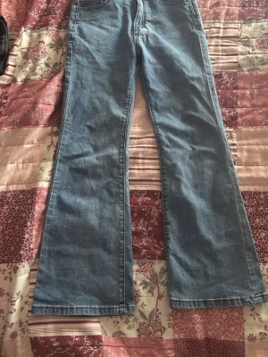 Blå bootcut jeans med hög midja - Snygga blå bootcut jeans med hög midja och klassisk femficksdesign. Jeansen har utsvängda ben och är tillverkade i ett mjukt denimtyg som ger en avslappnad och trendig look. Perfekta för dig som gillar retrovibbar och vill ha ett par jeans som sticker ut.