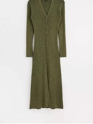 Olivgrön ribbad långklänning - Snygg olivgrön långklänning med ribbad struktur och v-ringning. Klänningen har långa ärmar och knappar hela vägen framtill, vilket ger en stilren och trendig look. Perfekt för dig som gillar en bekväm men ändå chic stil.