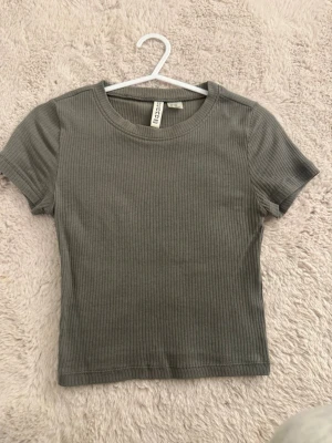 Ribbad t-shirt - Snygg grön ribbad t-shirt från H&M (Divided). Modellen är kortärmad med rund halsringning och har en tight passform. Perfekt till jeans eller kjol för en enkel och stilren look.
