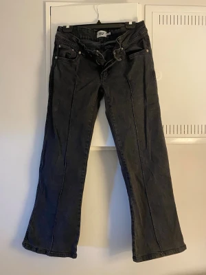 Svarta bootcut jeans från 157 - Säljer ett par svarta bootcut jeans från 157 med hög midja och klassiska fem fickor. Jeansen har pressveck längs benen och vida benslut för en retro vibe. Tillverkade i denim med en snygg tvättad finish och bälteshällor i midjan.
