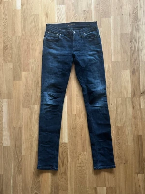 Nudie Jeans - Säljer ett par mörka Nudie Jeans. Slim jeans i modellen Tight Long John. Storlek W28 L34. De är i mycket bra skick utan defekter.
