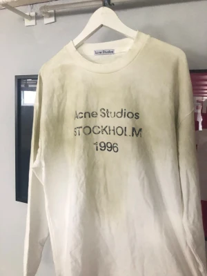 Vit sweatshirt Acne Studios Stockholm - Vit långärmad sweatshirt från Acne Studios med trycket 'STOCKHOLM 1996' framtill. Oversized passform och rund halsringning. Perfekt för en avslappnad streetwear-look.