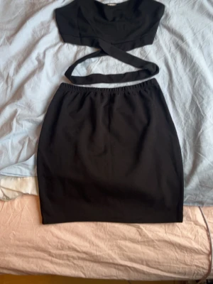 Svart body och kjol-set från SHEIN - Säljer ett svart set från SHEIN som består av en body med korsande band över magen och en matchande kjol med elastisk midja. Materialet är mjukt och stretchigt, perfekt för att skapa en snygg och trendig look.