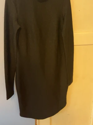 Svart långärmad klänning - En stilren svart klänning med lång ärm och rak passform. Klänningen är enkel och tidlös, perfekt för dig som gillar minimalistisk stil. Materialet ser ut att vara mjukt och stretchigt, vilket gör den bekväm att bära.