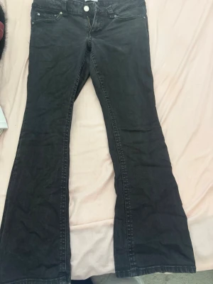 Svarta bootcut jeans med fickdetalj - Snygga svarta bootcut jeans med klassisk femficksdesign och en extra ficka med lock bak. Jeansen har utsvängda ben och normalhög midja. Perfekta för dig som gillar en retroinspirerad look.