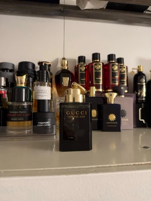 Gucci Intense Oud parfym - Gucci Intense Oud är en lyxig parfym i en elegant svart glasflaska med gulddetaljer och guldig kork. Flaskan har en stilren, fyrkantig form och utstrålar exklusivitet. Perfekt för dig som gillar djupa, orientaliska dofter och vill ha något som sticker ut i parfymhyllan.