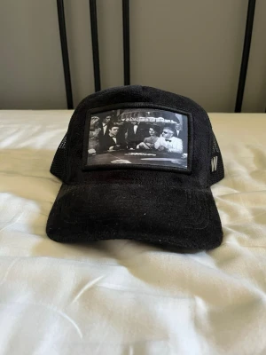 Svart keps med pokertryck från Ted Wonti - Svart keps med mesh på sidorna och böjd skärm. Framtill finns ett svartvitt tryck med pokerbordsmotiv och på sidan sitter en W-logga. Perfekt accessoar för en cool och avslappnad stil. Använd!!