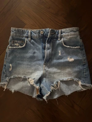 Jeans shorts från Zara med slitningar  - Högmidjade jeans shorts från Zara med slitningar i storlek 34.
