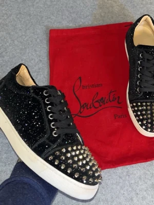 Christian Louboutin svarta sneakers - Svarta sneakers från Christian Louboutin med glittrande material och silverfärgade nitar på tån | medföljer även en ovanlig röd dustbag till dom | skick 9/10 2 nitar har trillat av men enbart använda på speciella tillfällen så inget annat synligt slitage | storlek 40, passar 41 | vid frågor och funderingar, tveka inte på höra av er☺️