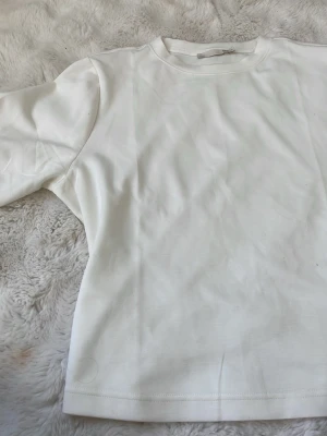 Vit basic t-shirt med rund hals - En stilren vit t-shirt med rund halsringning och korta ärmar. Modellen är rak och enkel, perfekt för att matcha med olika outfits. Tillverkad i mjukt material som känns skönt mot huden.