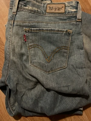 Levi's 571 ljusblå jeans - Ljusblå jeans från Levi's modell 571 med klassisk femficksdesign, tydliga slitningar och kontrastsömmar. Jeansen har en rak passform och är tillverkade i denim med en vintagekänsla. Perfekta för en avslappnad och trendig stil.