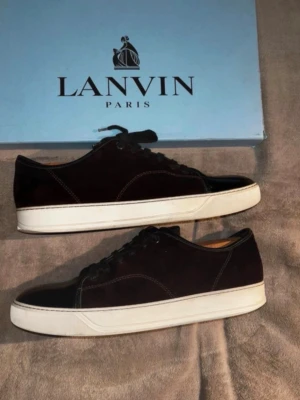 Vinröda Lanvin sneakers i mocka - Snygga svarta sneakers från Lanvin i mocka med vita sulor och svarta skosnören. Klassisk låg modell med stilren design och diskreta sömmar. Perfekta för dig som gillar minimalistisk och exklusiv stil.