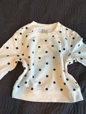 Plocka dot sweatshirt - Säljer en vit sweatshirt med svarta prickar. Tröjan har rund halsringning, långa ärmar och ribbade muddar vid ärmslut och nederkant. Perfekt för dig som gillar lekfulla mönster och en avslappnad stil.