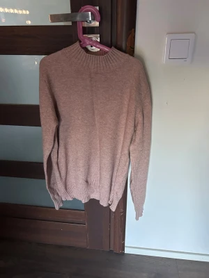Beige stickad tröja med hög krage - Mysig rosa stickad tröja med hög ribbad krage och ribbade muddar vid ärmslut och nederkant. Perfekt för lager-på-lager och enkel att matcha med jeans eller kjol. Tröjan har en rak passform och är tillverkad i ett mjukt material. I storlek M