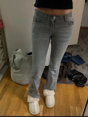 Grå bootcut jeans med låg midja - Snygga grå jeans med bootcut passform och låg midja. Jeansen har klassiska fem fickor och stängs med dragkedja och knapp. Perfekta för en avslappnad och trendig look.