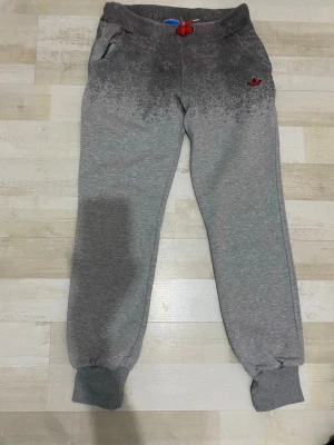 Grå Adidas mjukisbyxor med röd logga - Det står xxl, men jag tror det skulle passa storlek  L. Snygga grå mjukisbyxor från Adidas med en cool mörkare dip dye-effekt upptill och röd Adidas-logga på vänster sida. Byxorna har resår och röd dragsko i midjan samt muddar vid bensluten. Perfekta för en avslappnad och sportig stil.