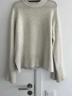 Beige stickad tröja - Mysig oversized stickad tröja i beige med bred ribbstickad kant vid ärmslut, nederkant och halsringning. Tröjan har en avslappnad passform och långa ärmar, perfekt för kyliga sommarkvällar 