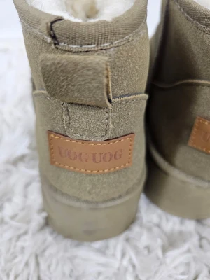 Beige UOG UOG fodrade boots - Säljer ett par beige boots från UOG UOG med mjukt, vitt foder på insidan. Skorna har en rund tå, låg skaft och är tillverkade i mockaliknande material. Perfekta för kalla dagar när du vill hålla fötterna varma och bekväma.