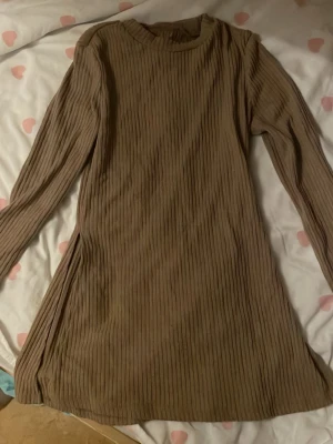 Beige ribbad långärmad tröja - Ribbad beige lång tröja med lång ärm och rund halsringning. Modellen är kort och har en slits på sidan för extra stilpoäng. Perfekt för dig som gillar en enkel men trendig look.