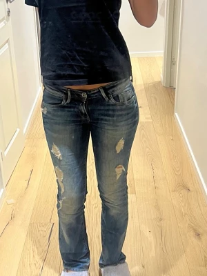Mörkblå slitna jeans - Snygga mörkblå jeans med slitningar på låren och knäna. Jeansen har raka ben, klassisk femficksdesign och låg midja. Perfekta för en avslappnad och trendig look.
