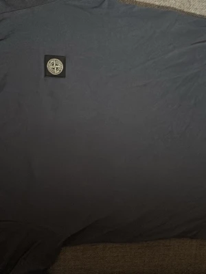 Mörkblå t-shirt från Stone Island - Snygg mörkblå t-shirt från Stone Island med klassisk logotyp-patch på bröstet. Enkel och stilren design som passar perfekt till jeans eller shorts. Tillverkad i mjuk bomull för en skön känsla hela dagen. Hör av er vid fler frågor.