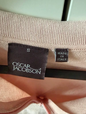 Ljusrosa polotopp från Oscar Jacobson - Säljer en ljusrosa polotopp från Oscar Jacobson, tillverkad i Italien. Toppen har korta ärmar, klassisk krage och ribbade muddar vid ärmslut och nederkant. Perfekt för dig som gillar stilrena och mjuka plagg.