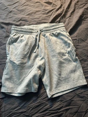 Gråa mjukisshorts med snörning - Snygga och bekväma grå mjukisshorts med elastisk midja och snörning. Shortsen har två sidofickor och är perfekta för en avslappnad stil. Tillverkade i mjukt bomullsmaterial som känns skönt mot huden.