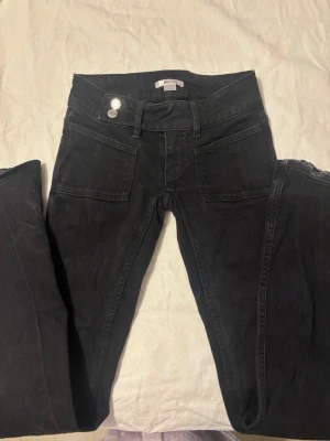 Svarta jeans med strassdetaljer bak - Snygga svarta jeans med raka ben och två stora fickor fram. Baktill finns två fickor med glittrande strassdetaljer i form av dubbla C. Jeansen har dubbla silverknappar i midjan och är tillverkade i ett stretchigt denimtyg.