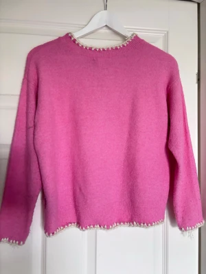 Rosa stickad tröja med vit kant - Säljer en söt rosa stickad tröja med vit dekorativ kant. Köpt från Sellpy men den var för liten så aldrig använt.❣️