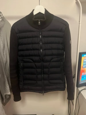 pufferjacka från Moncler - Snygg marinblå pufferjacka från Moncler med quiltad front och släta ärmar. Jackan har hög krage, tvåvägsdragkedja och två fickor med dragkedja. Perfekt för kalla dagar och har en stilren look med diskret Moncler-logga på ärmen.